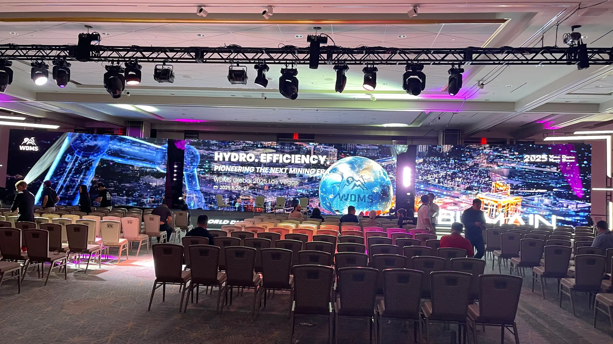 The WDMS Global 2025 general session at Resorts World Las Vegas: stage lights up and three LED screens lit as the audience comes in
